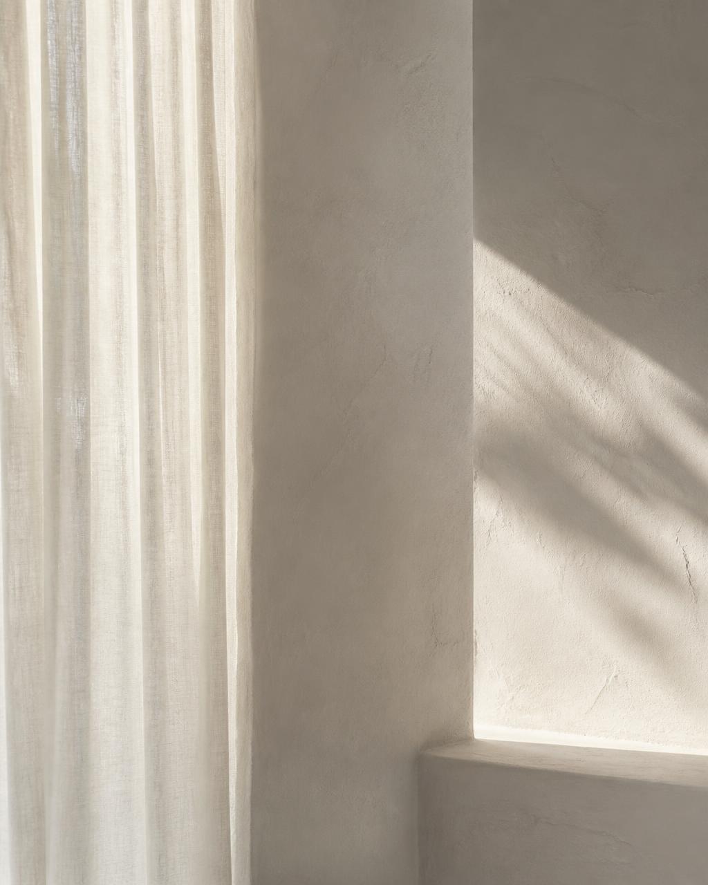 Soft daylight through a linen curtain against a pale plaster wall
